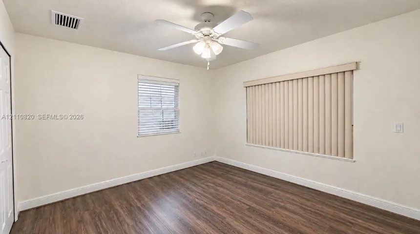 Wood-finish flooring, white ceiling fan with integrated light fixture, and windows equipped with neutral vertical and horizontal blinds