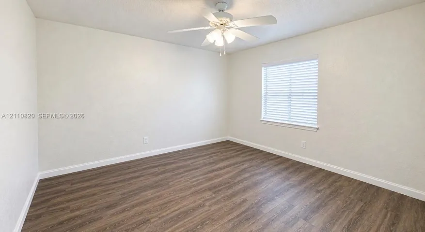 Neutral interior featuring wood-finish flooring, crisp white walls, a multi-light ceiling fan, and a window with horizontal blinds