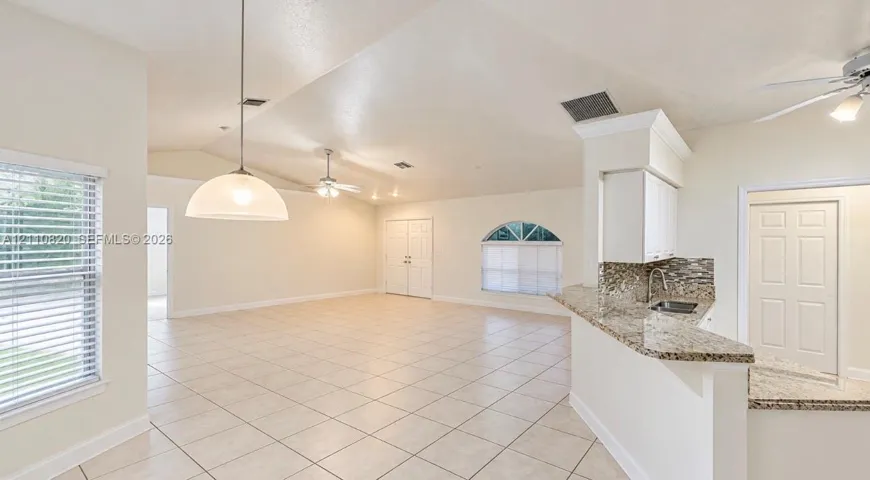 Open-concept space featuring vaulted ceilings, neutral floor tile, a stone-surface breakfast bar with integrated sink, and an arched window