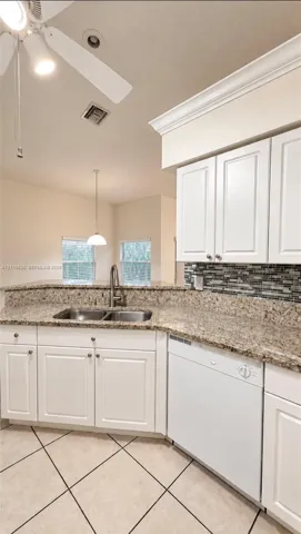 Kitchen featuring white shaker-style cabinetry, stone-surface countertops, mosaic tile backsplash, double-basin stainless steel sink with pull-down faucet, and diagonal-set ceramic tile flooring