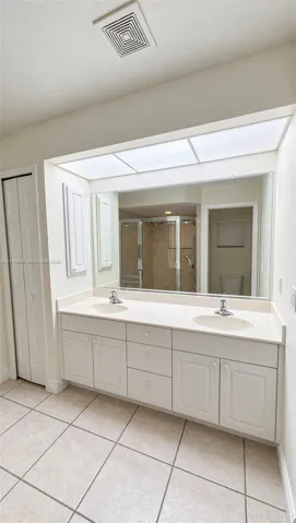 Dual-sink vanity with a solid-surface countertop, expansive integrated mirror, recessed ceiling lighting, and ceramic tile flooring