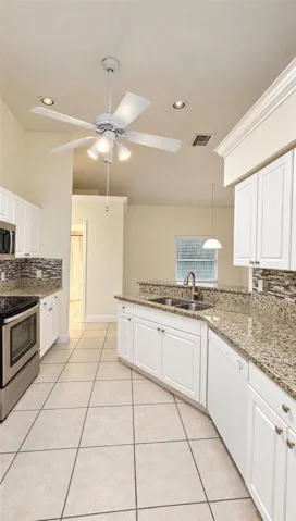 Kitchen featuring white cabinetry, stone countertops, multi-toned tile backsplash, stainless steel appliances, and tile flooring