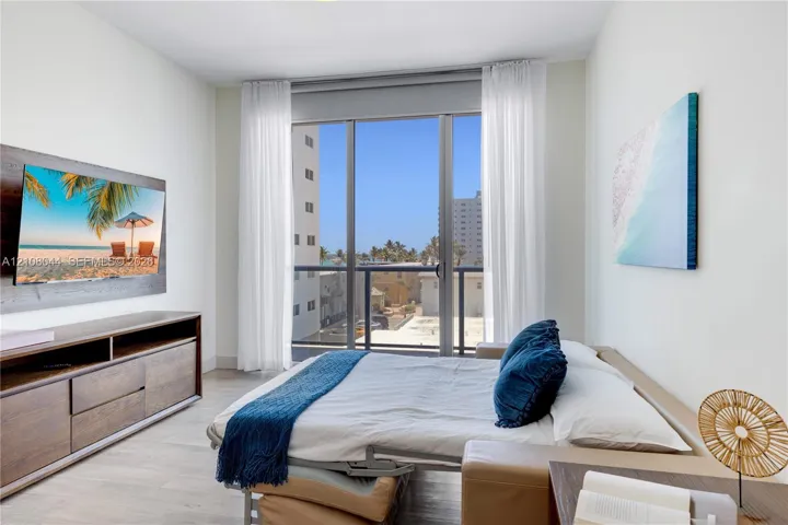 Floor-to-ceiling glass sliding doors opening to a balcony, light-toned wood-finish flooring, and crisp neutral wall finish