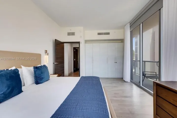 Floor-to-ceiling glass sliding doors with balcony access, wood-finish flooring, built-in floor-to-ceiling cabinetry, and solid-core interior doors