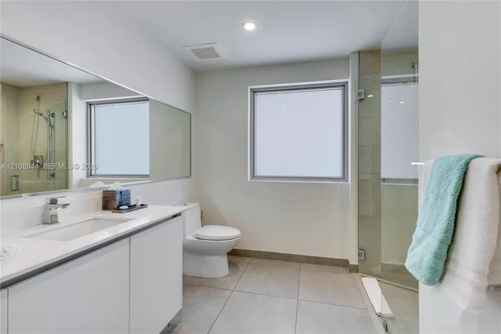 Bathroom featuring a vanity with a white countertop and rectangular undermount sink, a large wall-mounted mirror, a walk-in shower with a glass door, and large-format tile flooring
