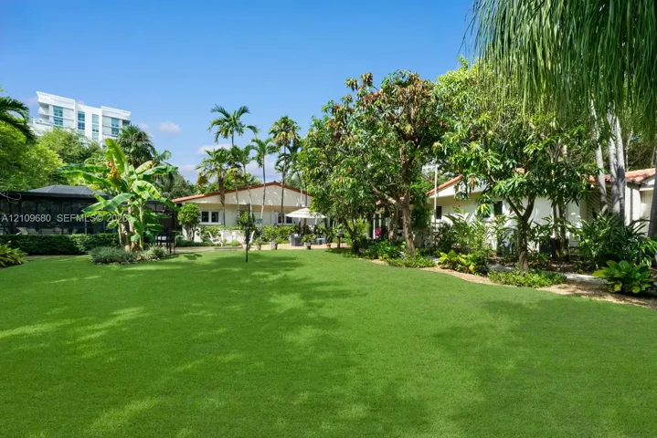 Expansive green lawn featuring mature trees, tropical foliage, and a screened outdoor structure