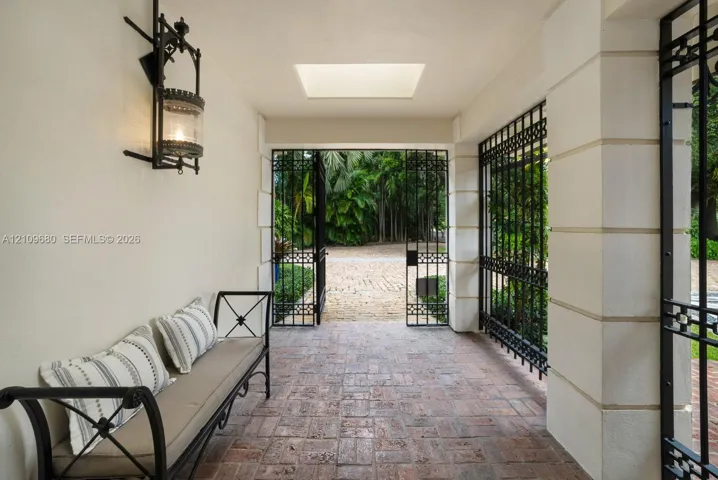 Covered entryway featuring brick-paver flooring, decorative wrought iron security gates, recessed ceiling lighting, and ornate wall-mounted lantern fixtures