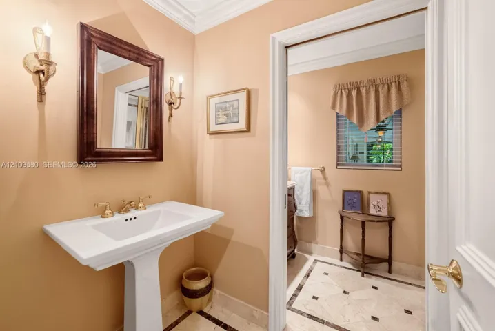 Powder room featuring a white pedestal sink with brass-finish widespread faucet, wall-mounted candle-style sconces, and stone tile flooring with decorative accent inlays