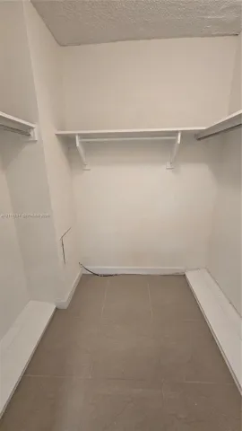 Walk-in storage space featuring neutral tile flooring and multiple built-in shelving and hanging rods