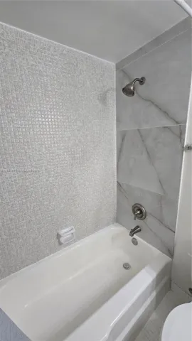 Bathtub with integrated shower, featuring textured mosaic tile accent wall, large-format stone-pattern wall tile, and metallic hardware