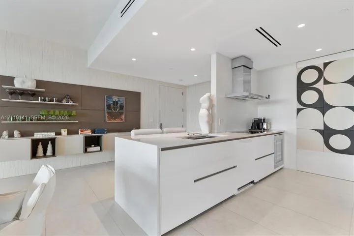 Modern kitchen featuring a central island with countertop, sleek handle-less cabinetry, stainless steel range hood, recessed ceiling lighting, and tile flooring