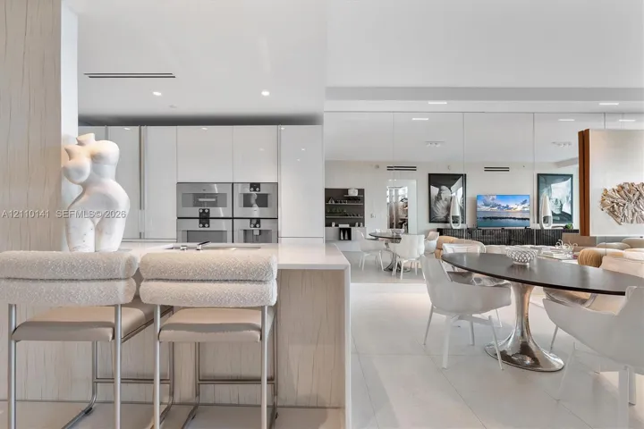 Modern kitchen featuring high-gloss cabinetry, stone-surface waterfall island, built-in dual stainless steel oven- microwave- integrated coffe sysstem for qulaity experience