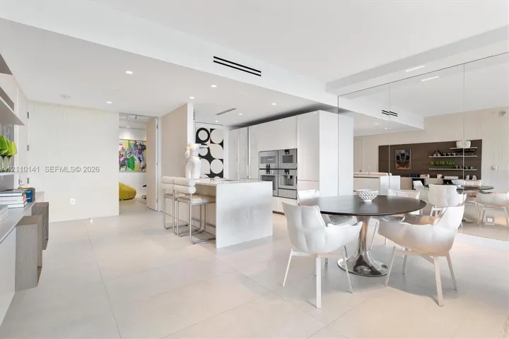 Contemporary kitchen featuring white slab-panel cabinetry, a central island with integrated stone waterfall-edge countertop, Large pantry