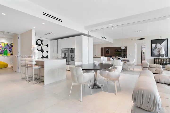 Contemporary interior featuring large-format tile flooring, high-gloss flat-panel cabinetry, a waterfall-edge kitchen island, integrated stainless steel appliances, and mirrored wall panels