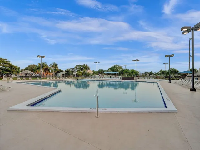 Large swimming pool with a concrete pool deck, metal safety railing, and integrated lighting poles