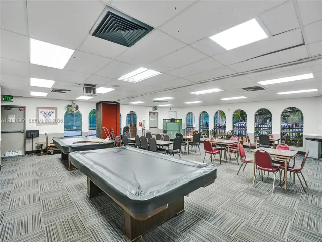 Large multipurpose room featuring a drop ceiling with integrated rectangular lighting, carpet tile flooring, and multiple arched windows