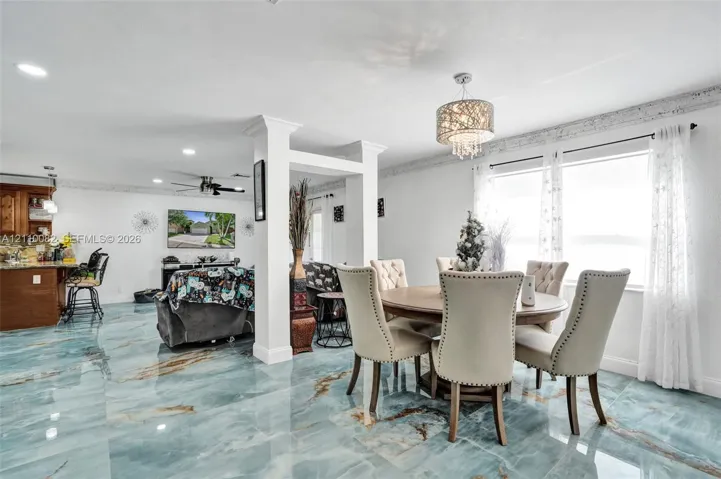Large-format polished tile flooring, recessed ceiling lighting, decorative tiered crystal chandelier, and custom structural columns