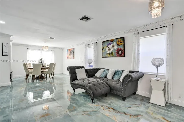 Open-concept area featuring polished stone-finish floor tiling, intricate crown molding, and tiered crystal-style pendant lighting