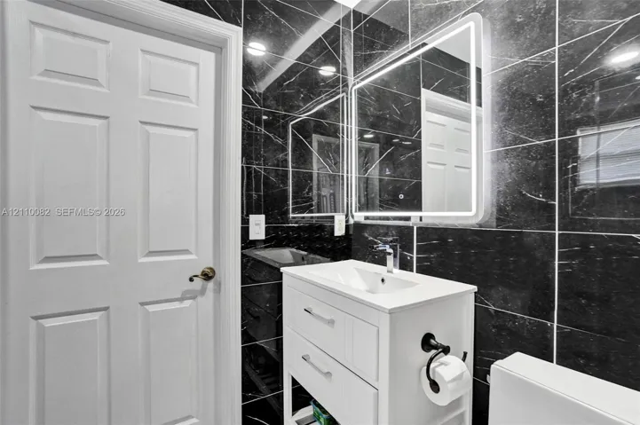 White vanity cabinet with an integrated basin, sleek chrome faucet, LED-backlit mirror, and full-height black stone-finish wall tile