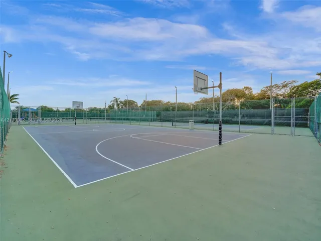 Outdoor sport court featuring a hard surface, dual basketball hoops, integrated perimeter fencing, and overhead light fixtures