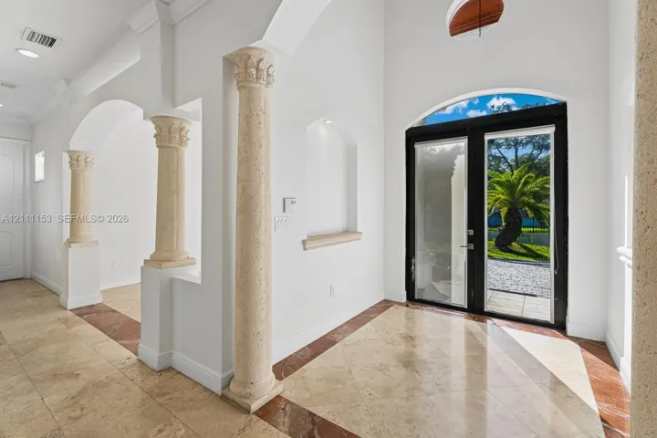 Foyer featuring high ceilings, stone columns with decorative capitals, stone flooring with decorative inlays, recessed wall niches, and double entry doors with a transom window