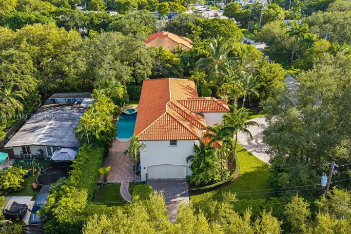 Two-story residence featuring a tile roof, paved driveway, attached garage, in-ground pool with integrated spa, and mature landscaping