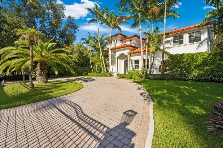 Stucco exterior featuring a terracotta tile roof, arched entryway, paved driveway, and mature palm landscaping