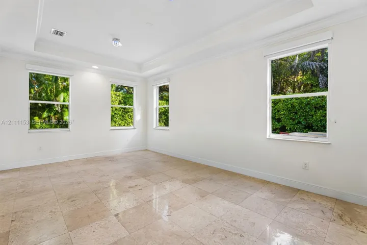 Spacious room featuring neutral tile flooring, a recessed tray ceiling, and four double-hung windows