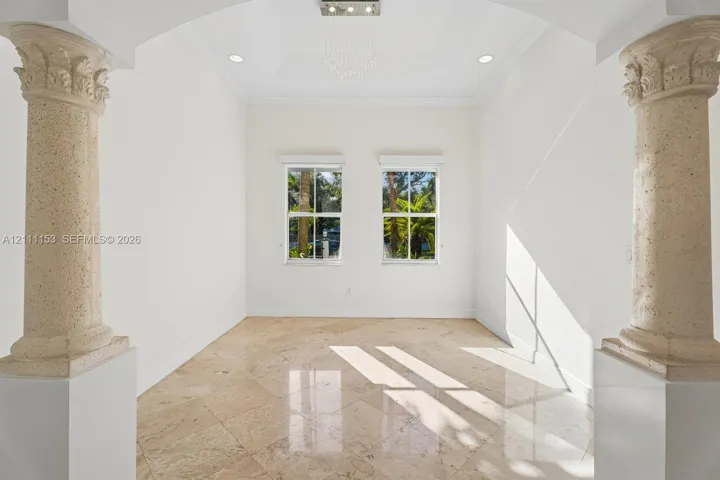 Architectural space defined by decorative stone columns, polished stone flooring, a tray ceiling with recessed lighting, and dual windows