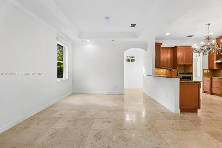 Tray ceiling with crown molding, stone tile flooring, arched entryway, wooden cabinetry, and peninsula-style countertop