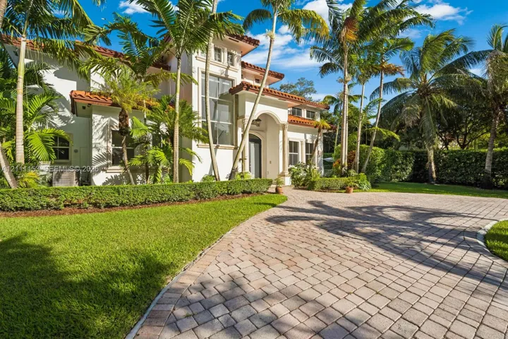 Mediterranean-style residence featuring a stucco facade, red tile roof, arched entryway with decorative columns, and an expansive paved driveway