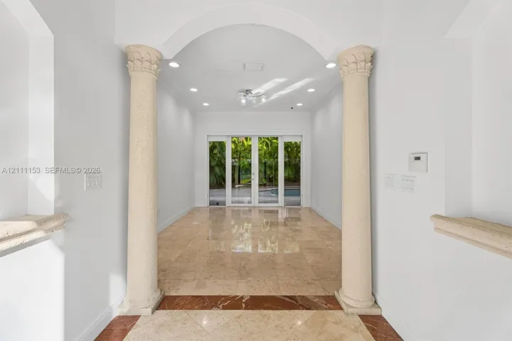 Entryway featuring arched architectural details, decorative stone columns, polished stone flooring with inlaid border, recessed lighting, and glass paneled doors