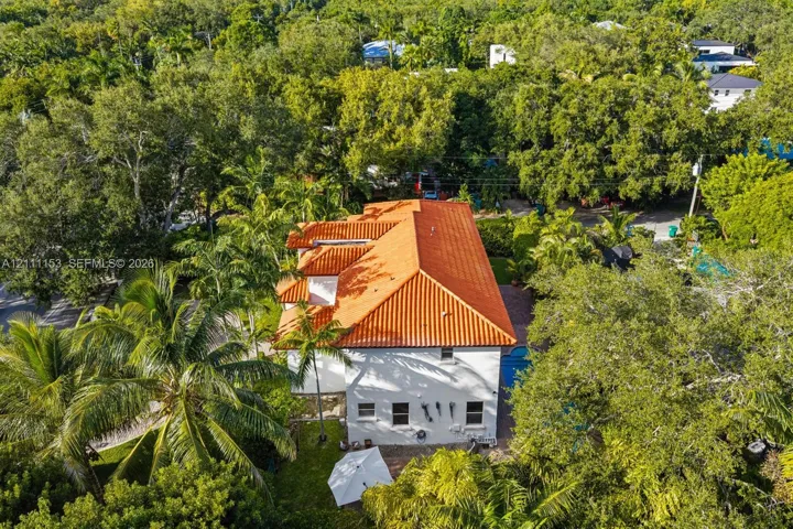 Two-story residence featuring a terracotta-tiled roof, white exterior stucco finish, and an integrated swimming pool situated within a heavily wooded lot