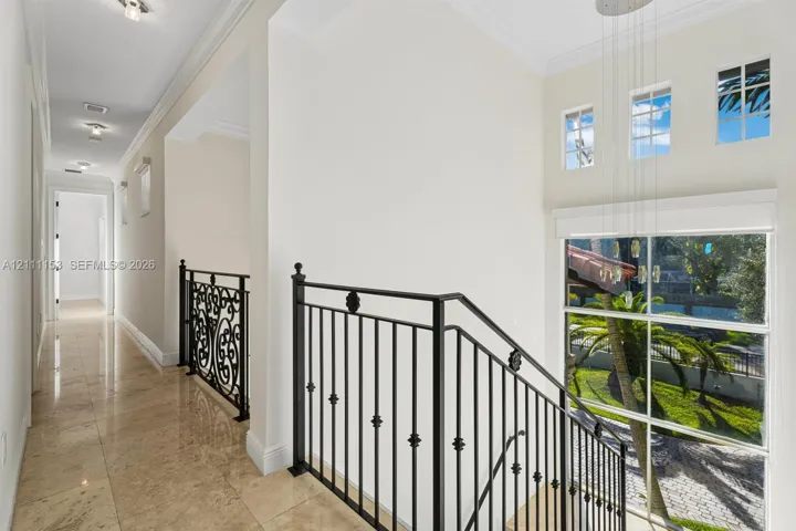 Neutral stone flooring, matte black wrought iron railings with decorative scrollwork, high ceilings, recessed lighting, and large windows featuring multi-pane glass
