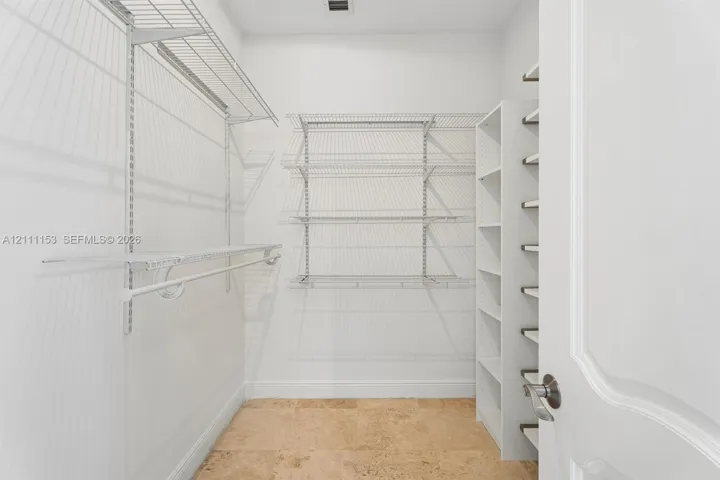 Storage area featuring stone tile flooring, white vertical built-in shelving, and adjustable metal wire rack shelving