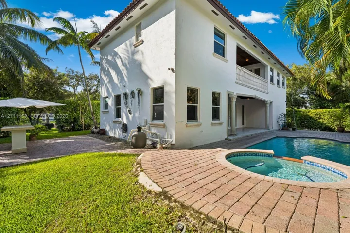 Stucco exterior residence featuring an integrated pool and spa, brick paver patio, second-story balcony, and manicured grounds
