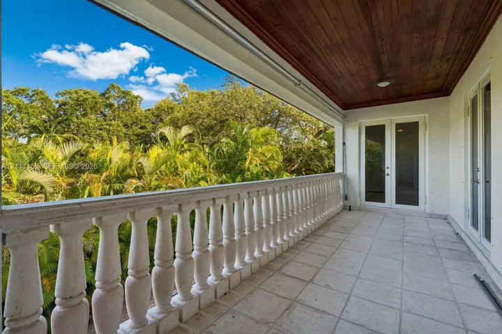 Covered balcony featuring stone-finish tile flooring, wood-plank ceiling, and decorative stone balustrade railings