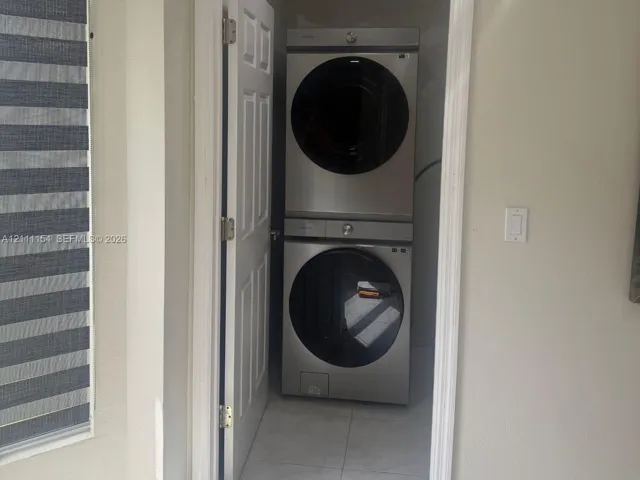 Stackable stainless steel laundry unit housed within a dedicated closet featuring neutral tile flooring and a white swing door
