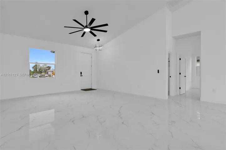 View toward the front door across the living area with cathedral ceiling and ceiling fan.