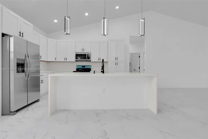 Large waterfall-edge quartz island with stainless steel refrigerator and full-height backsplash.