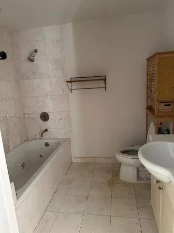 Bathroom featuring a jetted tub, wall-mounted shower fixture, ceramic tile surround, and ceramic floor tiling