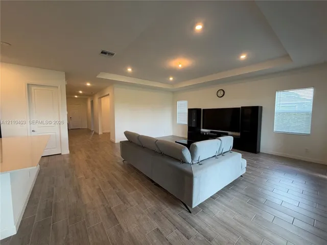 Open floor plan featuring a tray ceiling, recessed lighting, wood-finish flooring, and horizontal window blinds