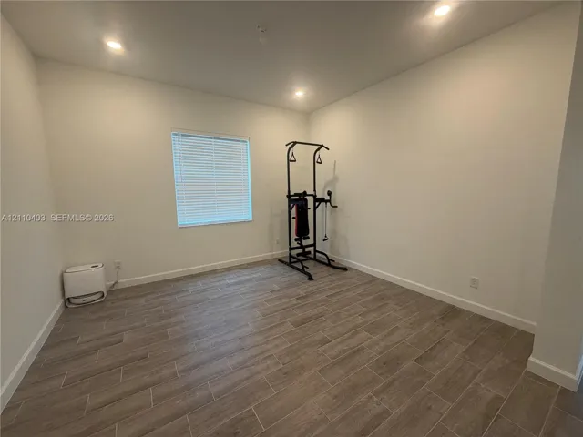 Neutral-toned interior space featuring wood-finish flooring, recessed lighting, and a single window with horizontal blinds