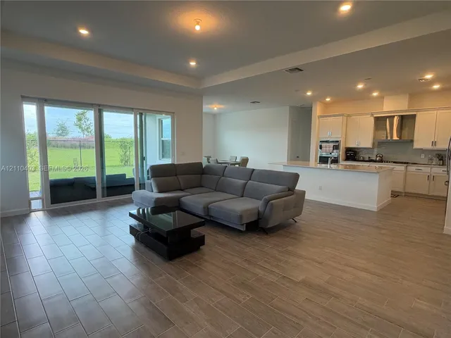 Open-concept space featuring wood-finish tile flooring, recessed ceiling lighting, a tray ceiling, sliding glass doors, and kitchen cabinetry with a built-in cooktop range