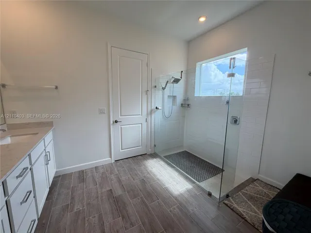 Walk-in shower with a glass enclosure, subway tile surround, and recessed shelving, paired with a vanity featuring a light-toned countertop and wood-finish tile flooring