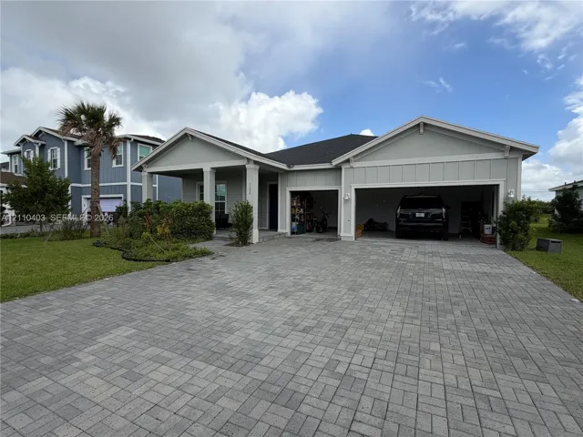 Single-story residence with a light-toned vertical siding exterior, covered front porch, multi-car garage, and paver driveway