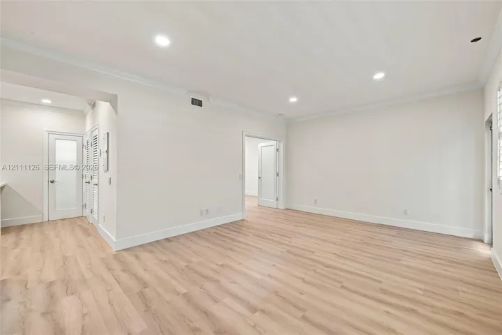 Spacious room featuring wood-finish flooring, recessed lighting, crown molding, and neutral wall color