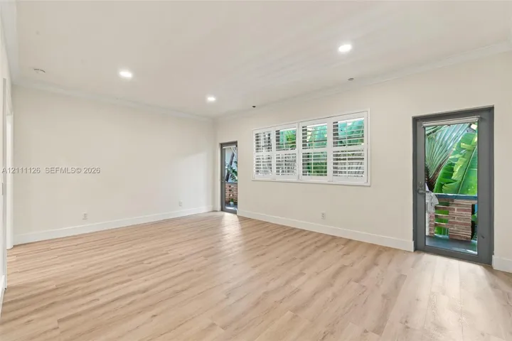 Spacious room featuring wood-finish flooring, recessed lighting, multi-pane windows with plantation shutters, and glass-paneled exterior doors