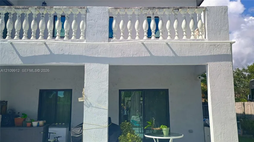 Stucco exterior featuring a covered patio, a second-story balcony with decorative balustrade, and dual glass sliding doors