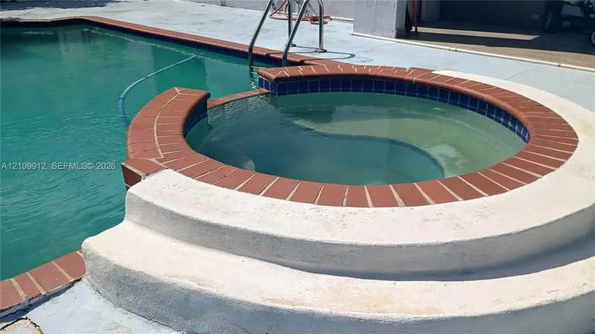 In-ground swimming pool featuring a circular spillover spa, brick coping, and concrete pool deck